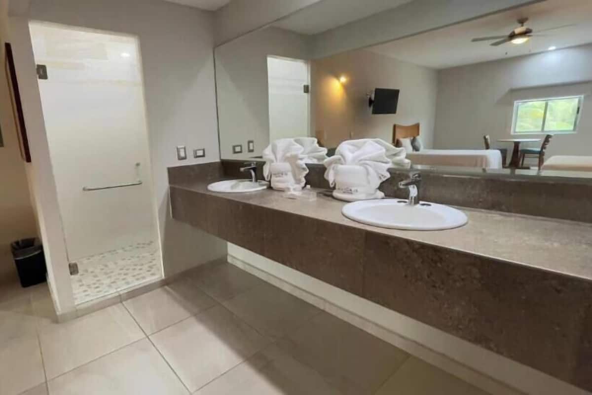 Une salle de bain dotée d’un grand miroir, de deux lavabos et d’un espace douche.
