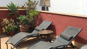 Een terras met twee loungestoelen, een kleine ronde tafel en diverse potplanten.