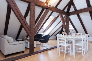 An attic room with exposed wooden beams, a sofa, two chairs, a dining table with chairs, and a small side table with a basket. - Hedera Estate, Hedera A5 - Breakfast included (Dubrovnik)