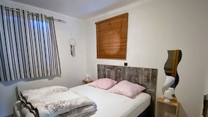 Un dormitorio con cama, mesita de noche, espejo, ventana con persianas e iluminación empotrada.