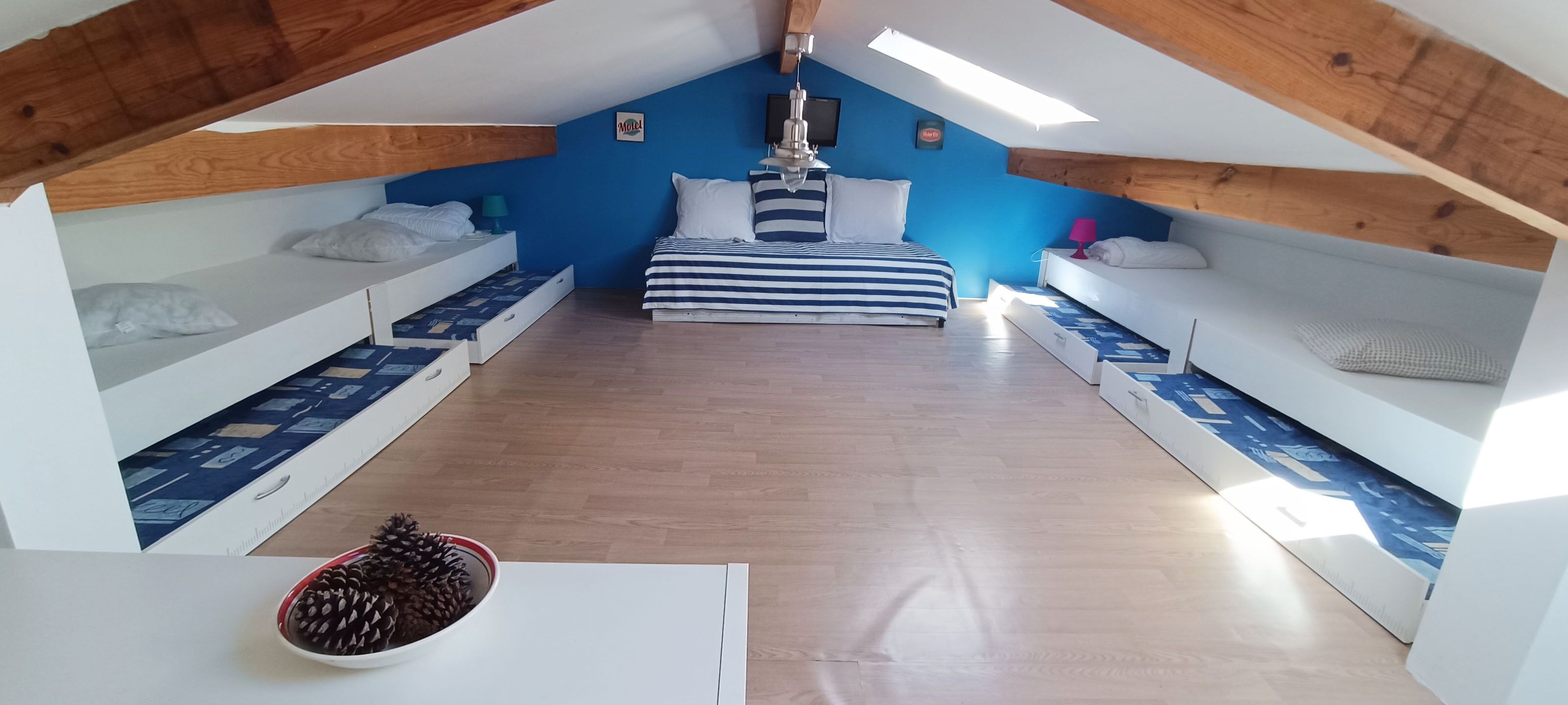 Un dormitorio de altillo pequeño y luminoso, con techo inclinado, ropa de cama a rayas y rincones de estar integrados.