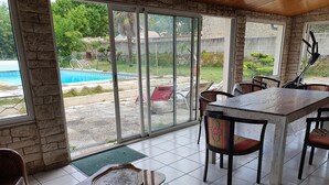 Eine sonnendurchflutete Terrasse mit Esstisch und Stühlen, Blick auf einen Swimmingpool und eine Steinmauer.