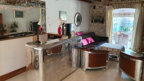 Ein rustikales Wohnzimmer mit freiliegenden Holzbalken, einer Steinwand, einem großen Spiegel, einem Sofa mit rosa Kissen und einem kleinen Holztisch.