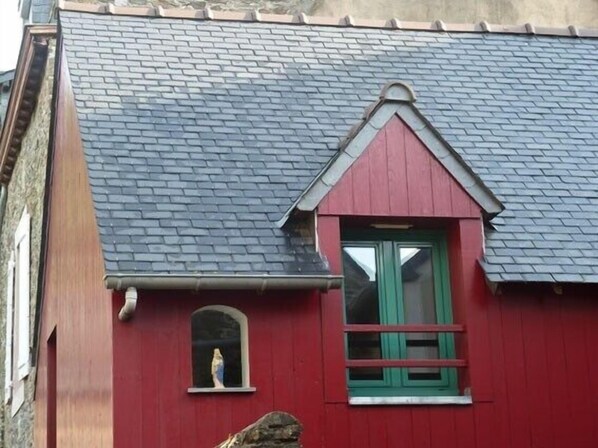 Ein rotes Gebäude mit dunklem Dach, einem kleinen Rundbogenfenster und einem größeren Fenster mit grünen Fensterläden.