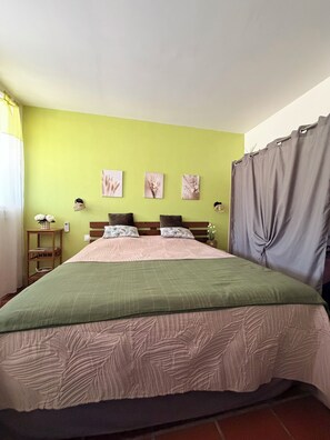 A bed with a green and beige bedspread, a wooden headboard, and three wall-mounted pictures.