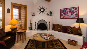Uma sala de estar aconchegante com lareira, uma mesa de centro com revistas, um sofá e uma luminária.