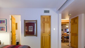 Um quarto com uma cama, uma porta de madeira e um corredor que dá para uma sala de jantar.