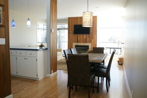 A modern kitchen with white cabinetry and a wooden countertop, a dining area with a wooden table and patterned chairs, and a large window providing natural light. - Carefree Days at The Beach (Watsonville)