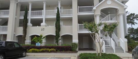 A multi-story building with a central courtyard, numbered 27, featuring balconies, a staircase, and a parking area.