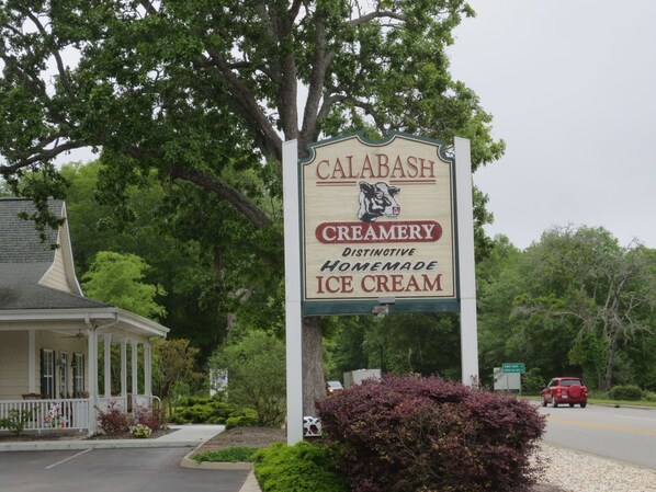 A creamery sign with a cow illustration, surrounded by trees and a house. - On The Golf Course! Steps From The Pool! 10 Minutes From Sunset Beach! (Calabash)