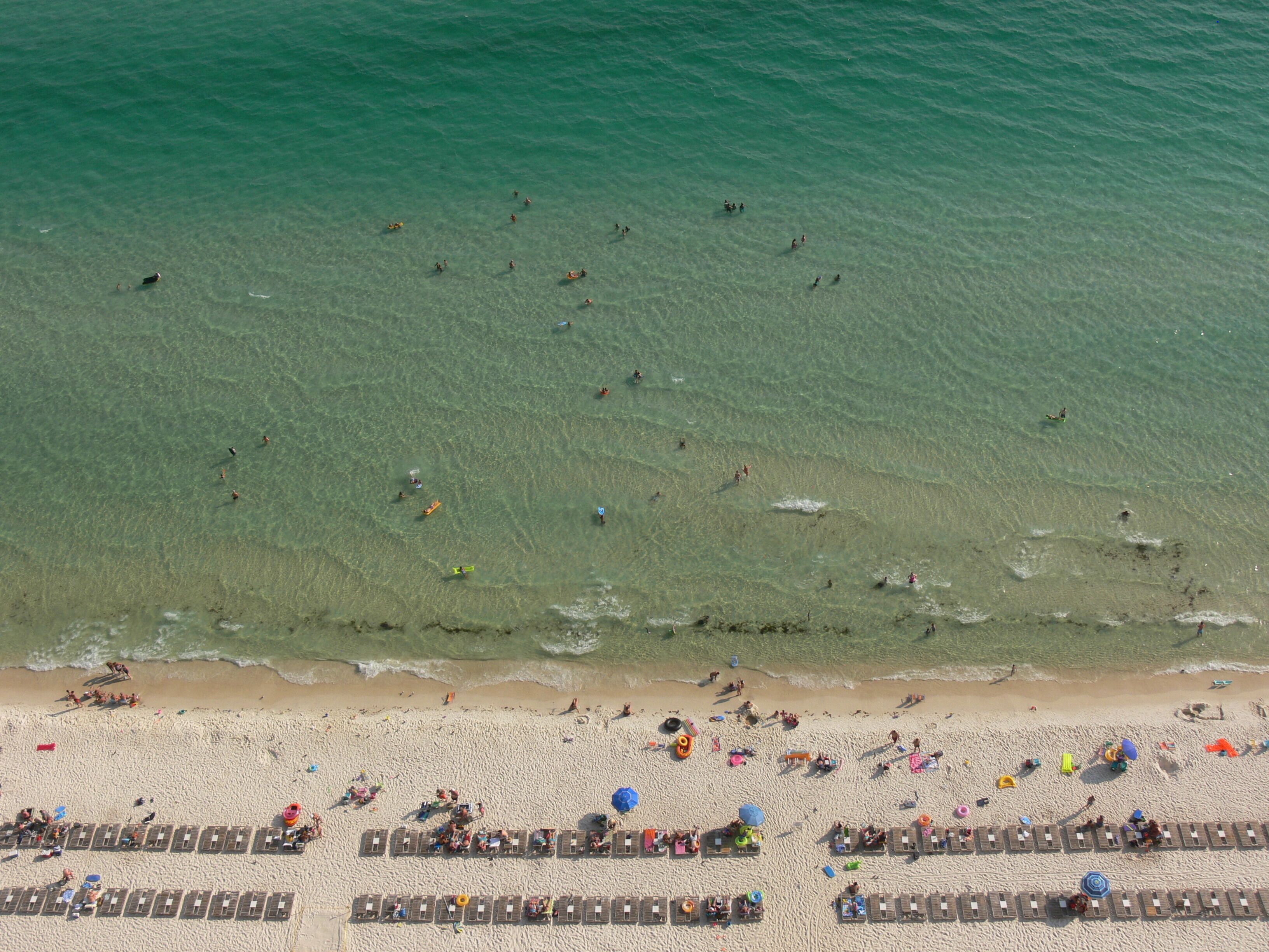 A beach with rows of sun loungers and umbrellas, and people swimming in the water.