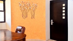 Une salle de conférence avec une table en bois et un fauteuil en cuir, une œuvre d’art décorative au mur et une porte sombre dotée d’un panneau lumineux.