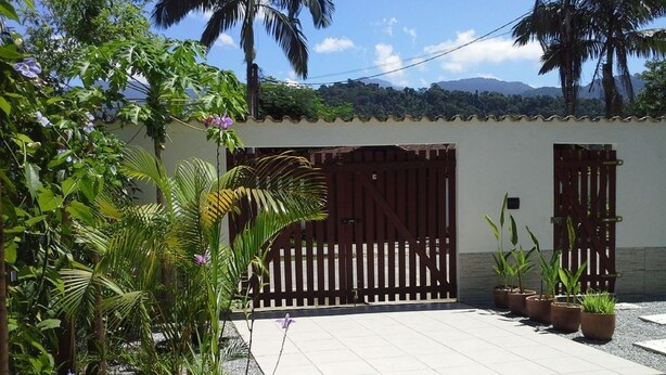 A courtyard with a tiled floor, a wooden gate, potted plants, and a white wall with a small window. - Casa Verde Paraty (Paraty)