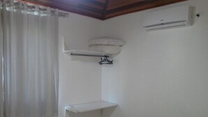 A bedroom with a bed, a bedside table, a hanging shelf, a window with curtains, and an air conditioning unit. - Casa Verde Paraty (Paraty)