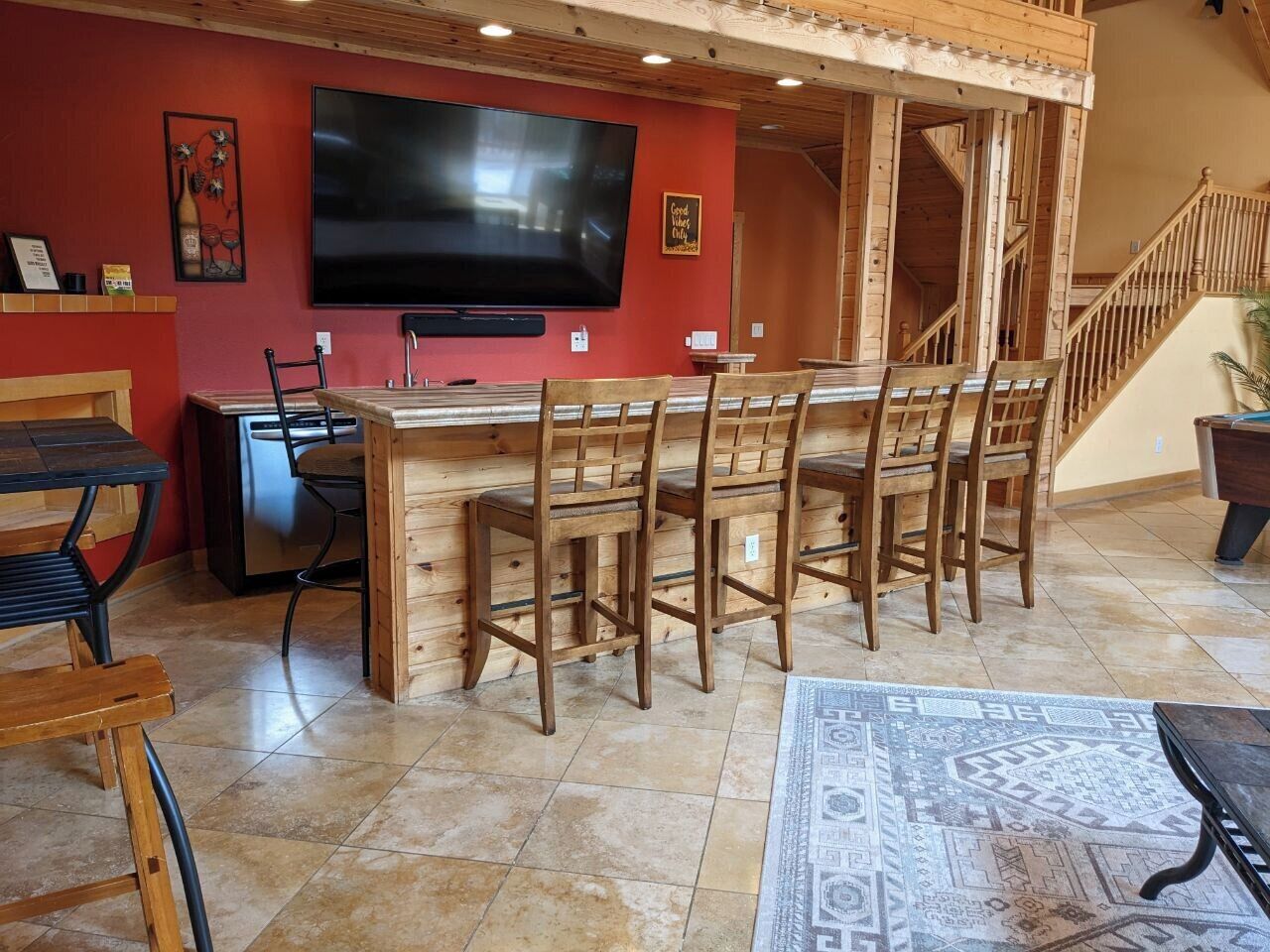 A bar area with wooden stools, a TV mounted on the wall, and a staircase leading to an upper level.