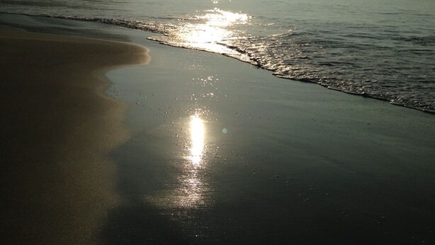 Ein Strand mit ruhiger See, blauem Himmel und Bergen in der Ferne.