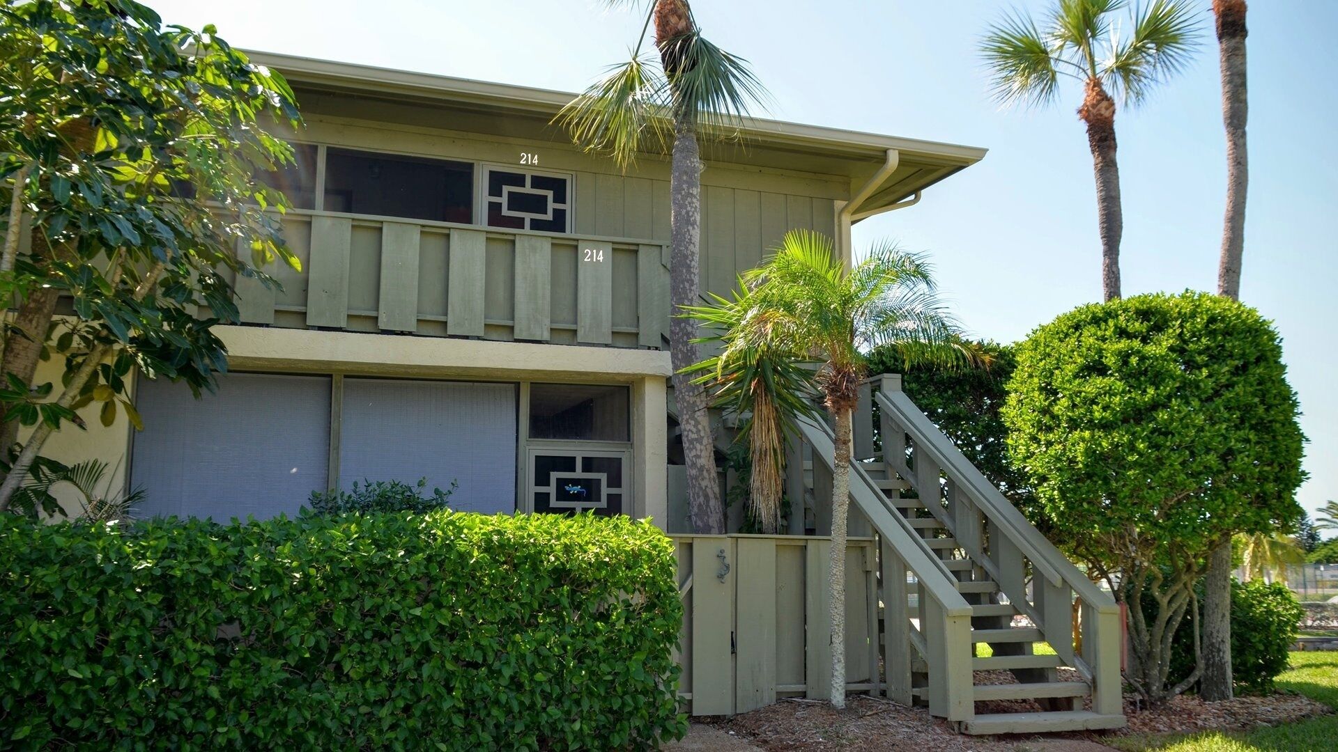 A two-story building with a balcony, a staircase, and palm trees.