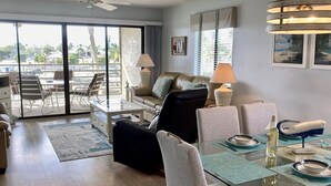 A spacious living room with a glass dining table set for two, a sofa, and a ceiling fan. - Westbay Point Moorings 214 2 Bedroom Condo by RedAwning (Holmes Beach)