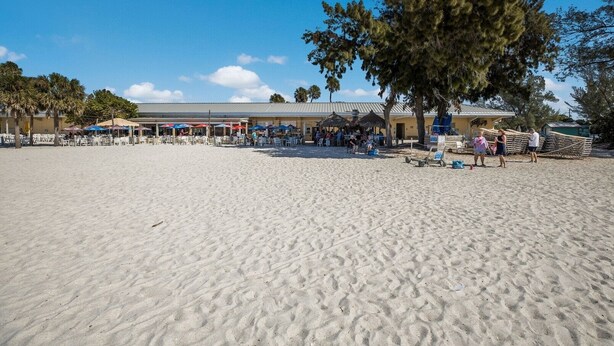A beachside restaurant with outdoor seating and umbrellas, surrounded by palm trees. - Westbay Point Moorings 214 2 Bedroom Condo by RedAwning (Holmes Beach)
