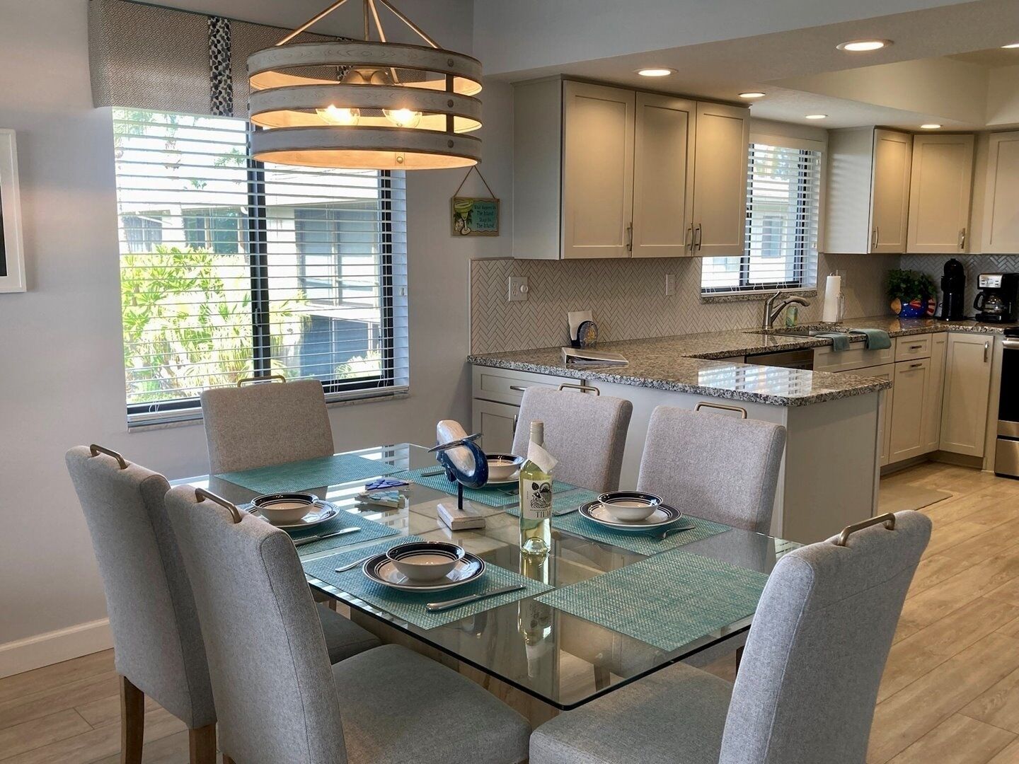 Una cocina moderna con comedor. Cuenta con una mesa de comedor con cubierta de vidrio y sillas, una isla de cocina integrada y una lámpara colgante sobre la isla.