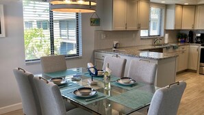 A modern kitchen with a dining area. It features a glass-top dining table with chairs, a built-in kitchen island, and a pendant light above the island. - Westbay Point Moorings 214 2 Bedroom Condo by RedAwning (Holmes Beach)