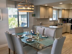Una cucina moderna con zona pranzo. Dispone di un tavolo da pranzo con piano in vetro e sedie, un'isola cucina integrata e una lampada a sospensione sopra l'isola.