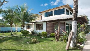 Una casa de dos pisos con fachada blanca, techo de tejas y un pequeño jardín delantero con palmeras y arbustos.