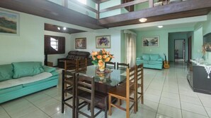 Amplia sala de estar con mesa de comedor de vidrio rodeada por sillas de madera, sofá color turquesa y un balcón con barandilla de madera.