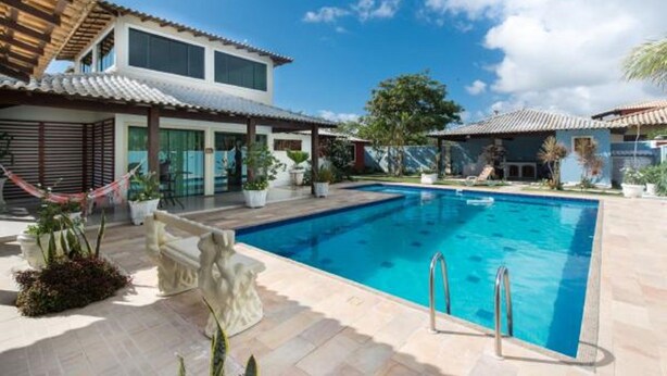 Una piscina con agua cristalina azul, rodeada de plantas en macetas y una terraza de piedra.