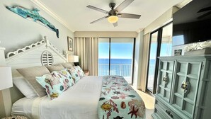 A bedroom with a bed, a ceiling fan, a TV, a balcony with a view of the ocean, and a dresser. - Shoalwater 1106 3 Bedroom Condo by RedAwning (Orange Beach)