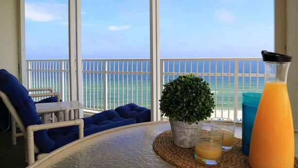 A balcony with a view of the ocean, a table with drinks, and blue seating. - Shoalwater 1106 3 Bedroom Condo by RedAwning (Orange Beach)