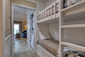 Una habitación con una cama litera, una puerta que da a un balcón y vistas a una sala de estar con un sofá y una lámpara.