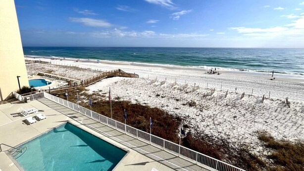 A beach view from a hotel balcony with a swimming pool and beach access.