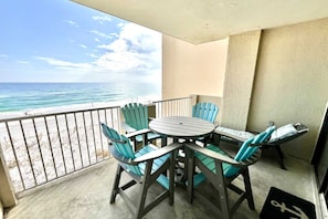 A balcony with a round table and chairs, overlooking a beach with the ocean and a clear sky.