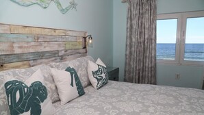 A bedroom with a wooden headboard, patterned bedding, and a view of the sea through a window.