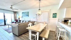 A spacious living area with a wooden dining table, a sofa, and a kitchen area with a countertop and bar stools.
