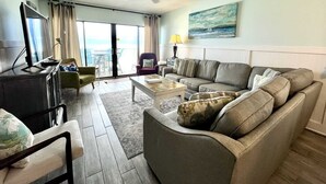 A living room with a sofa, armchairs, a coffee table, a TV, and a painting on the wall.