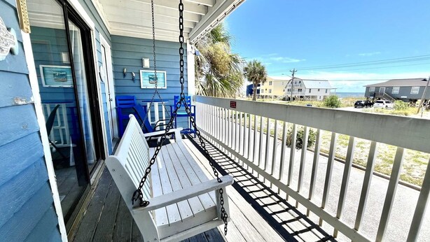 A porch with a swing chair, a white railing, and a view of the beach and ocean. - Sea Oats H102 2 Bedroom Condo by RedAwning (Gulf Shores)