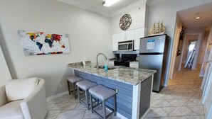 A modern kitchen with a central island, bar stools, a microwave, and a refrigerator. - Royal Palms 1306 1 Bedroom Condo by RedAwning (Gulf Shores)