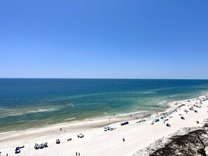 Ein Strand mit klarem, blauem Wasser, sandigem Ufer und Sonnenschirmen.