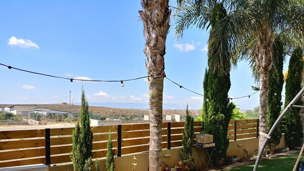 A patio with a table and chairs, surrounded by palm trees and a view of distant buildings. - Assaf's Cabin (Mateh Asher)