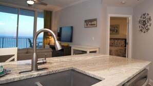 A modern kitchen with a large sink, a ceiling fan, and a view of the ocean through large windows. - Lighthouse 1017 1 Bedroom Condo by RedAwning (Gulf Shores)