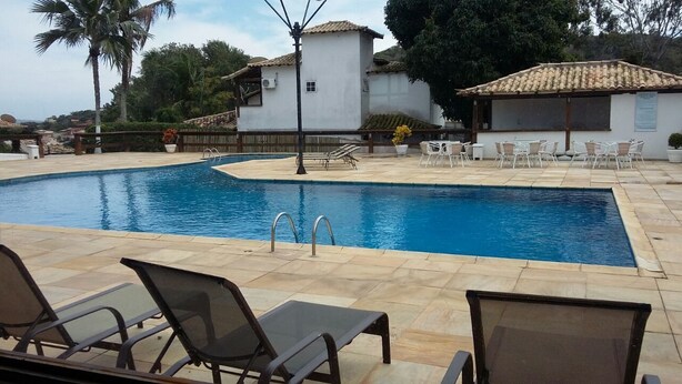 Una piscina con sillones de descanso y un edificio pequeño al fondo.