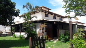 Una casa de dos pisos con techo de tejas, un porche cubierto y un jardín cuidado con diversas plantas y un portón de madera.