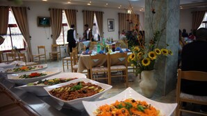 A buffet setup with various dishes, wooden chairs, and a vase with sunflowers. - St. Vincent Guest House - Bethlehem (Bethlehem)