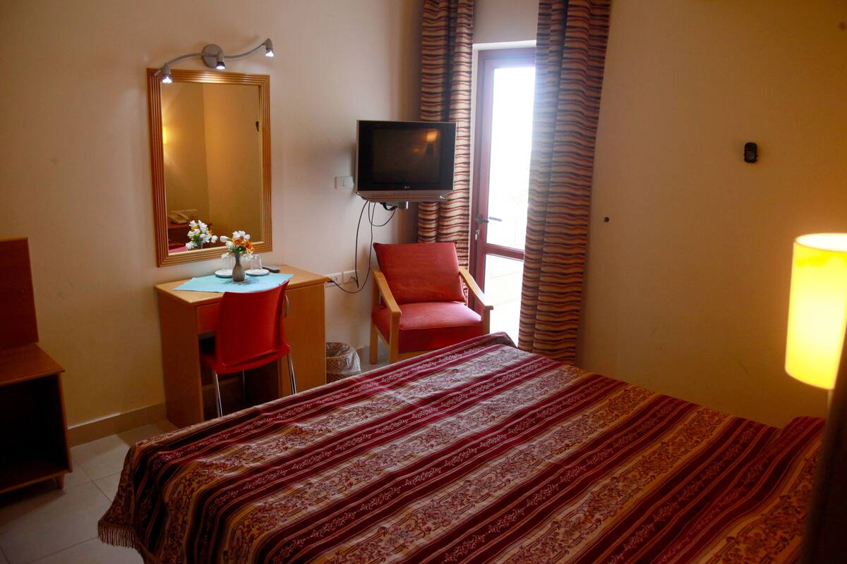 A hotel room with a bed, a desk with a chair, a television, and a window with curtains.