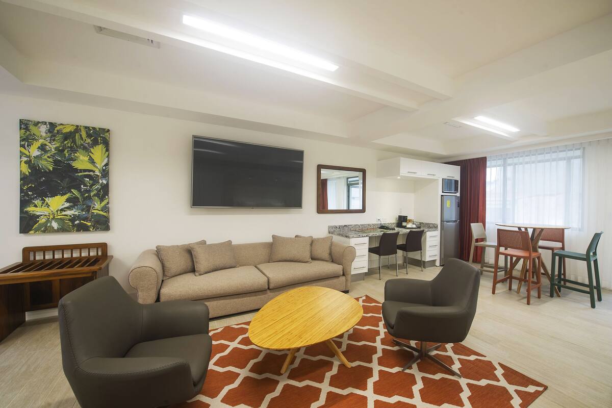 A modern living room with a sofa, two armchairs, a coffee table, and a dining area with a table and chairs.