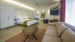 A modern hotel room with a bed, a sofa, a desk, and a TV. - Balmoral Suites (San José)