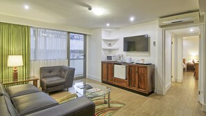 A modern living room with a leather sofa, a glass coffee table, and a TV mounted on the wall. - Balmoral Suites (San José)