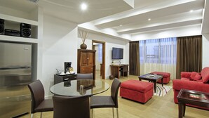 A modern living room with a glass dining table, red sofas, a TV, and a kitchen area with a refrigerator and microwave. - Balmoral Suites (San José)